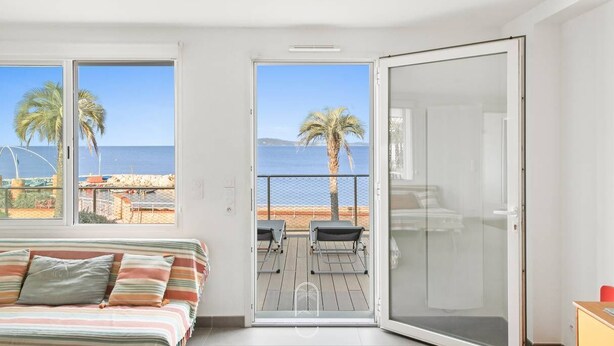 Een slaapkamer met een bed, een schuifdeur naar een balkon en uitzicht op het strand en de zee.