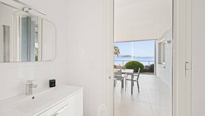 Een moderne badkamer met een witte wastafel, een spiegel en uitzicht op een terras met een tafel en stoelen.