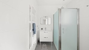 Een moderne badkamer met een douchecabine van glas, een wit wastafelmeubel met spiegel en een handdoekrek.