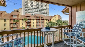 A balcony with a pool, outdoor seating, and a view of surrounding buildings.