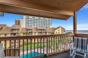 A balcony with a view of a swimming pool, a grassy area, and a tall building in the background. - 🌊 Ocean Front - Private Balcony - Anchorage II 305 ☀️ (Myrtle Beach)