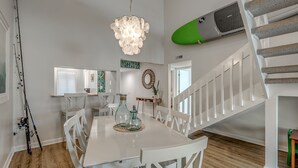 A dining area with a white table and chairs, a chandelier, and a staircase with white railings.
