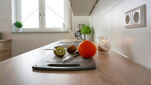 Une cuisine avec une planche à découper, des kiwis, une orange et un bocal en verre.