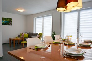 Un coin repas avec une table en bois dressée pour quatre personnes, entourée de chaises blanches.