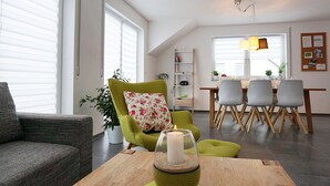 Un salon moderne avec un fauteuil vert, un canapé gris et un coin repas comprenant une table et des chaises en bois.
