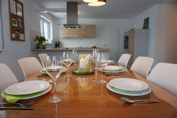 Une table à manger dressée pour six personnes, avec des assiettes blanches, des serviettes vertes et des verres à vin.