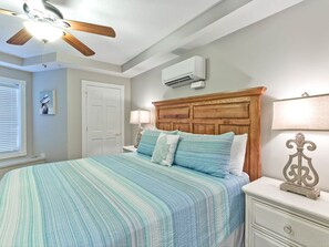 Een slaapkamer met een bed, houten hoofdbord, nachtkastjes, een airconditioning en een plafondventilator, en een raam met jaloezieën.
