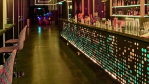 A modern bar area with neon lighting, seating, and a bar counter with bottles. - nhow Frankfurt (Frankfurt)