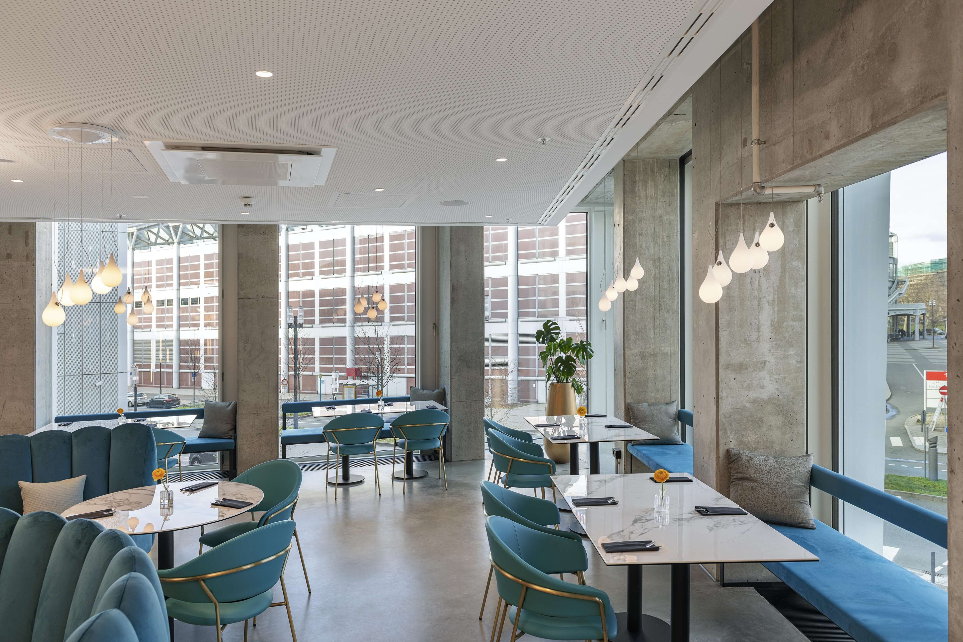Un restaurant moderne doté de hauts plafonds, de grandes fenêtres et proposant différents types de sièges, notamment des tables et des banquettes.