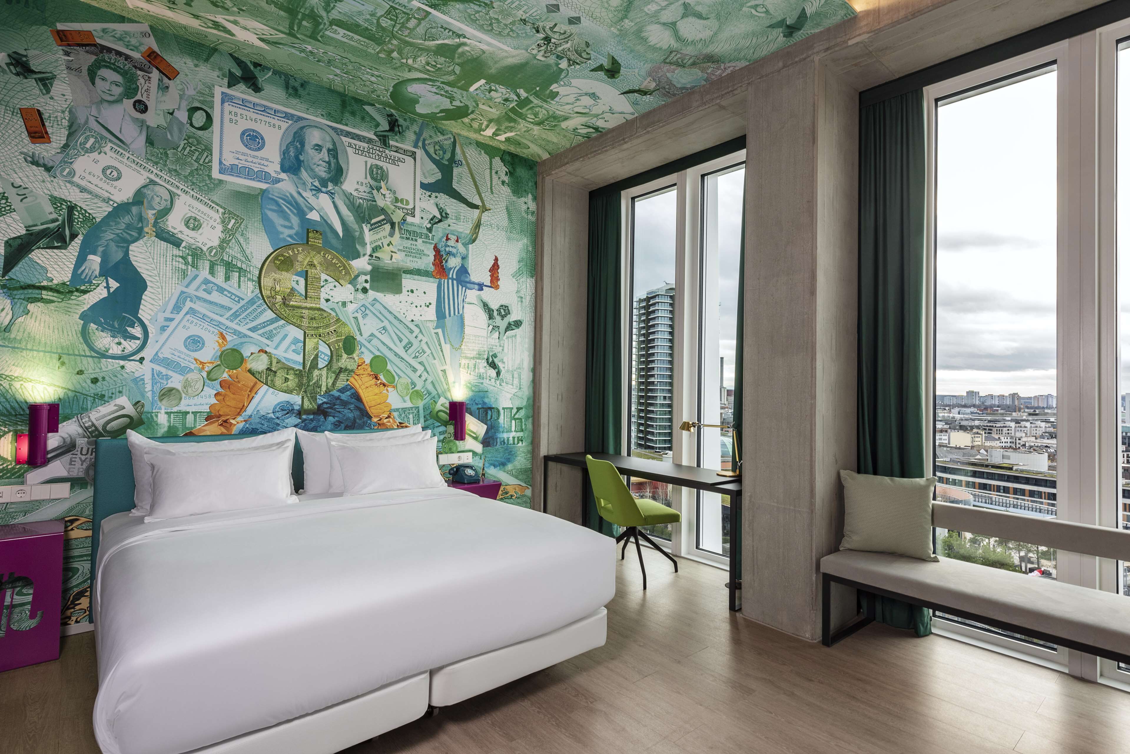A modern bedroom with a large bed, a desk, and a bench by the window. The room features a cityscape view.
