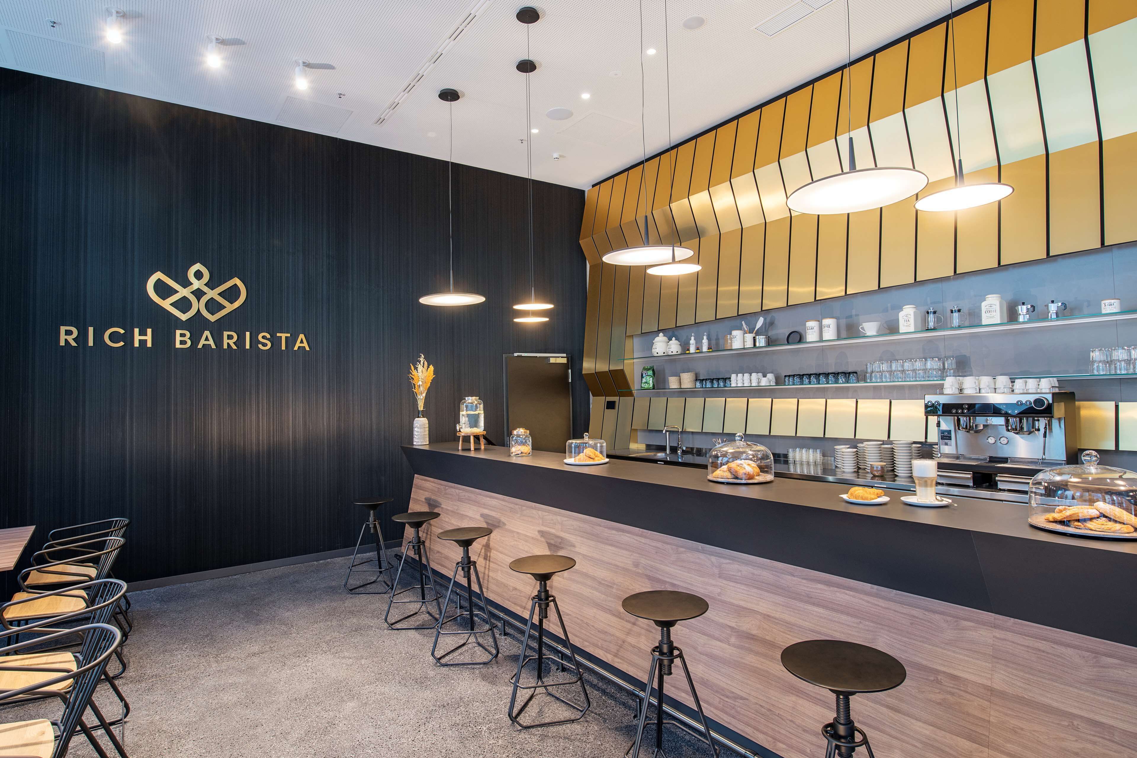 Una estación de barista moderna con un logotipo, taburetes, una máquina de café y una exhibición de pasteles.