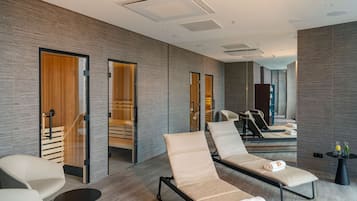 A modern hotel room with a large mirror, two lounge chairs, a small table, and a wooden door.