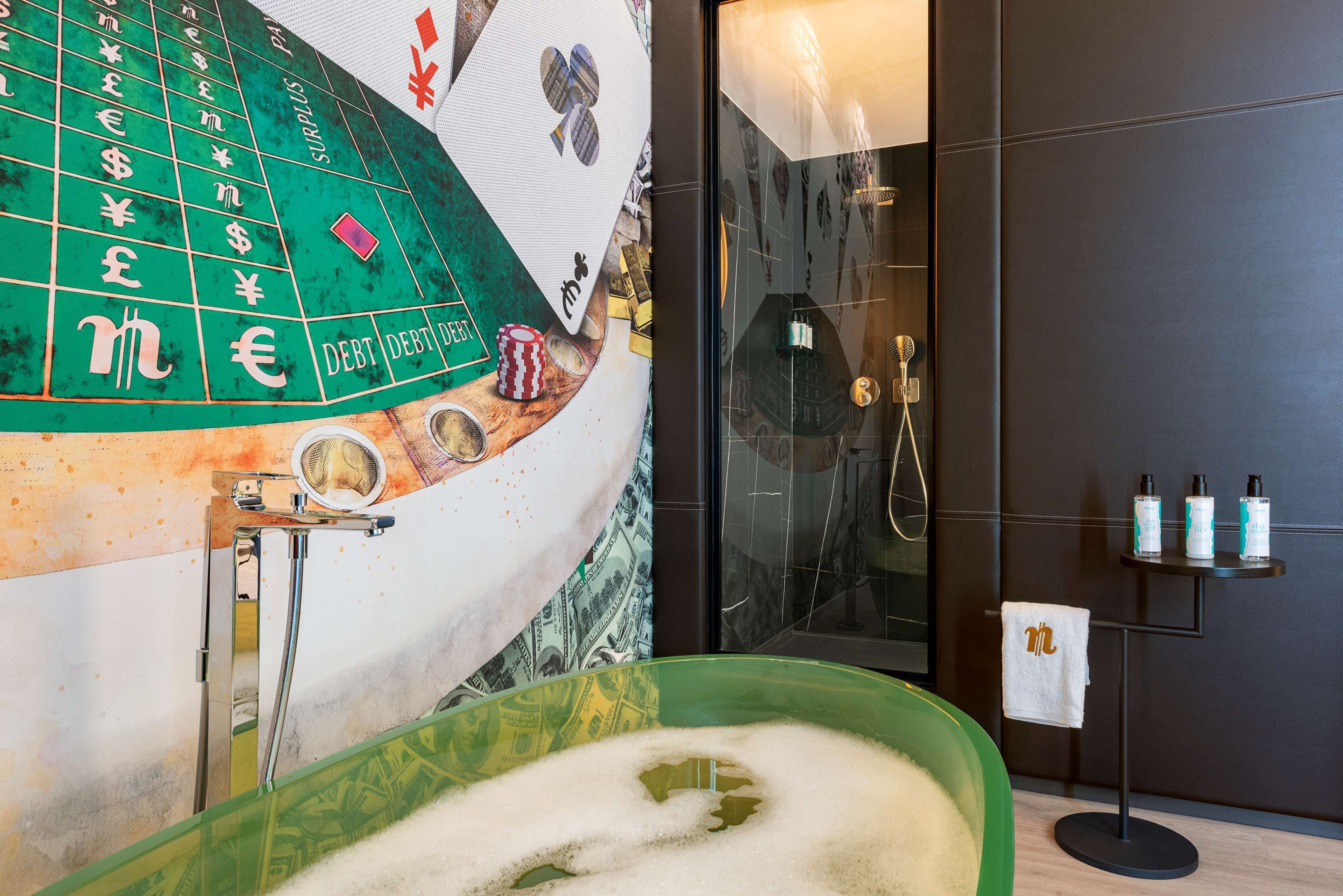 A bathroom with a green bathtub, a roulette wheel mural, a shower area, and toiletries on a small table.