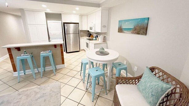 Una cocina compacta con armarios blancos, un refrigerador de acero inoxidable y una pequeña zona de comedor con una mesa redonda y taburetes.