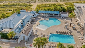 Vista aérea de un complejo turístico con dos piscinas, zonas de descanso y una terraza cubierta.