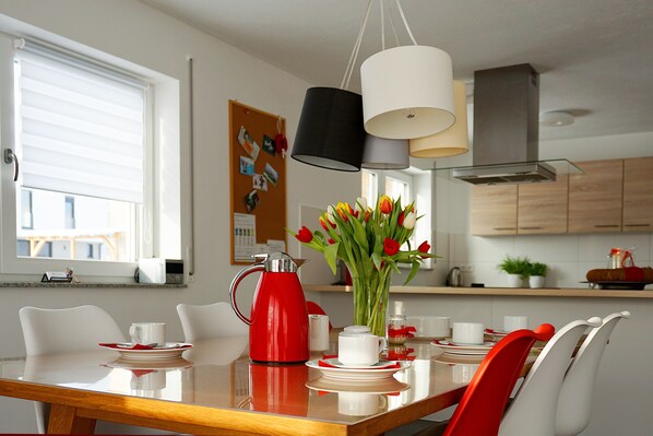 A modern kitchen with a dining table set for four, a red kettle, and a vase of tulips. - Spacious vacation apartment with terrace & 3 bedrooms on the Swabian Alb (Blaubeuren)
