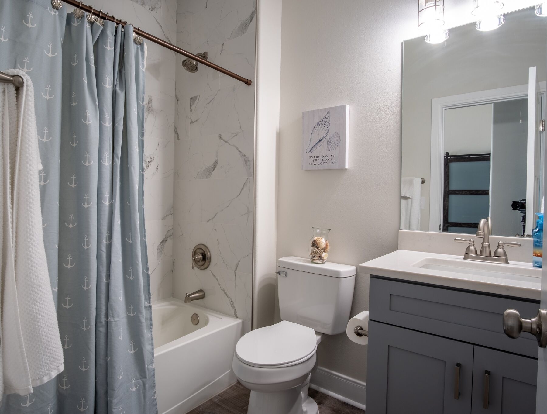 A bathroom with a bathtub, toilet, vanity, and a shower curtain with anchor patterns.