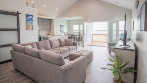 A spacious living area with a large beige sectional sofa, a ceiling fan, and a view of the kitchen and dining area. - Blue Haven – Waterfront Home w/ Heated Pool & Private Pier (Rockport)