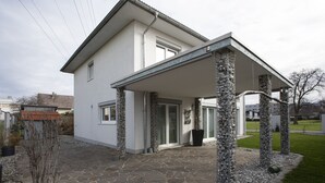 A modern house with a stone-paved entrance, a covered porch, and a stone column structure. - Great detached house near Lake Constance (Lauterach)