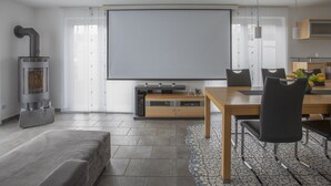 A modern living room with a fireplace, a large TV, a dining area with a table and chairs, and a kitchen area with a microwave. - Great detached house near Lake Constance (Lauterach)