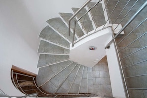 Stunning spiral staircase with a metal handrail and grey tile steps, leading to a door at the bottom.