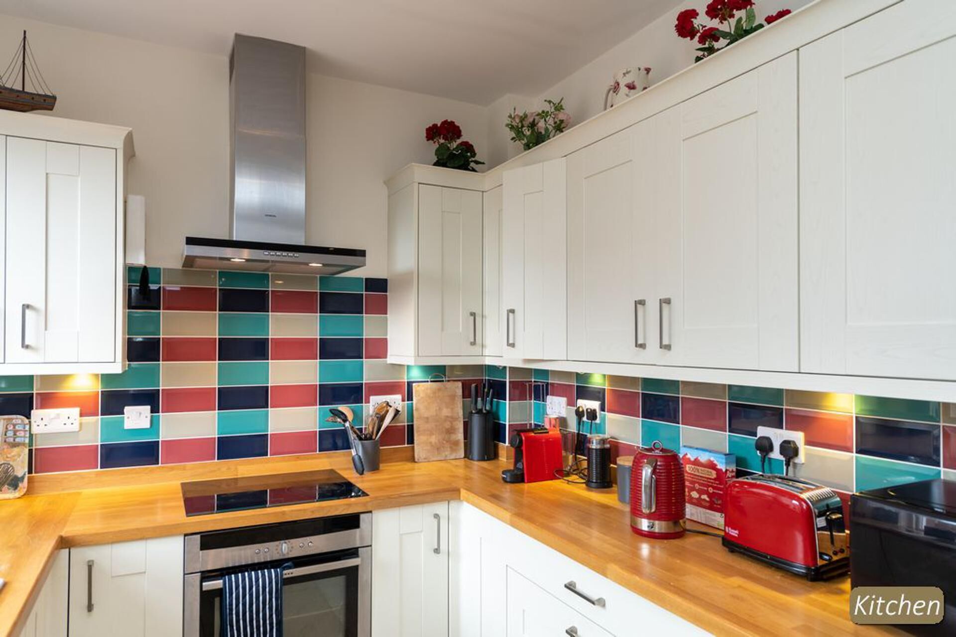 A modern kitchen with white cabinets, colorful backsplash tiles, stainless steel appliances, and a wooden countertop.
