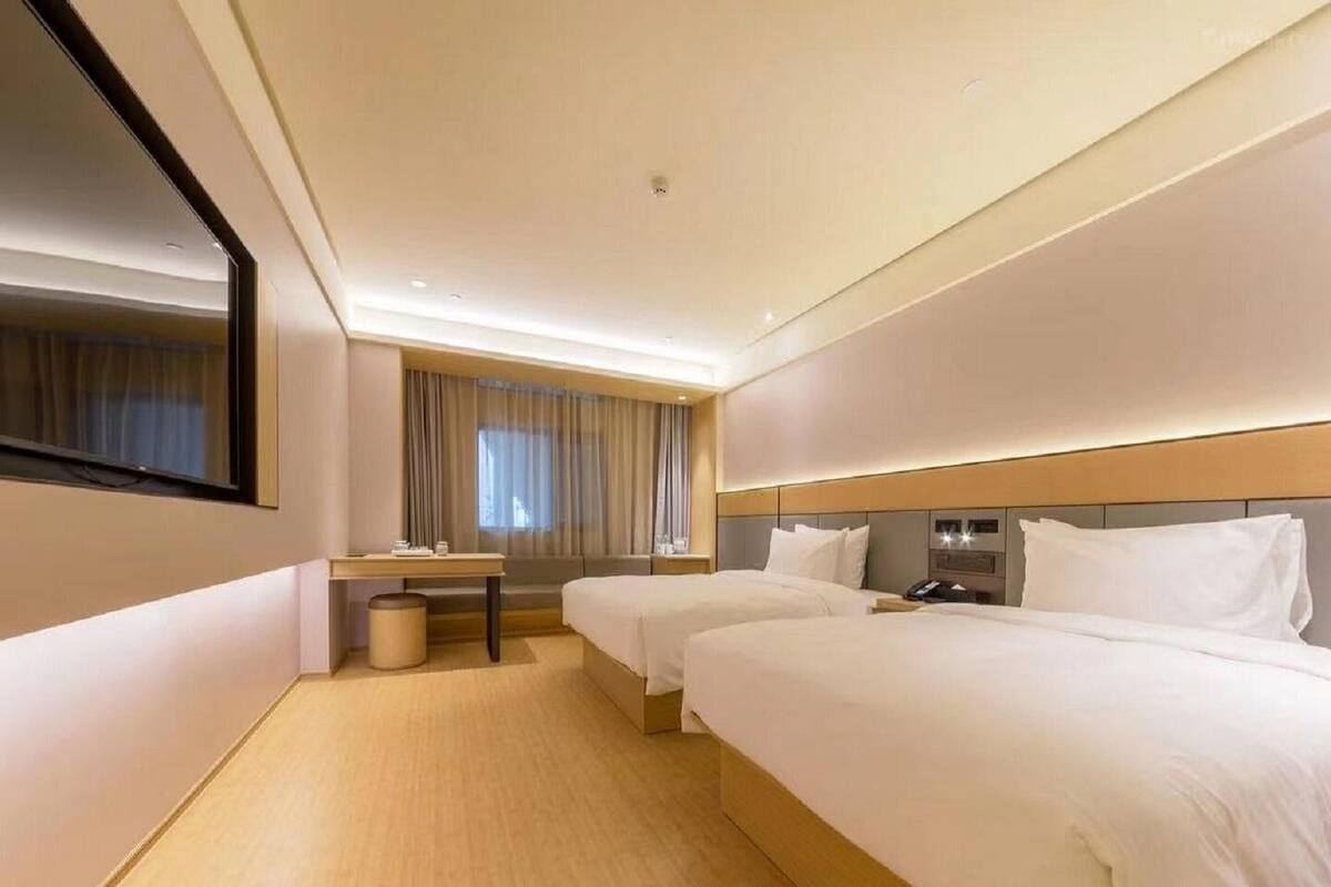 Habitación de hotel con dos camas, un escritorio, una silla y un espejo grande.