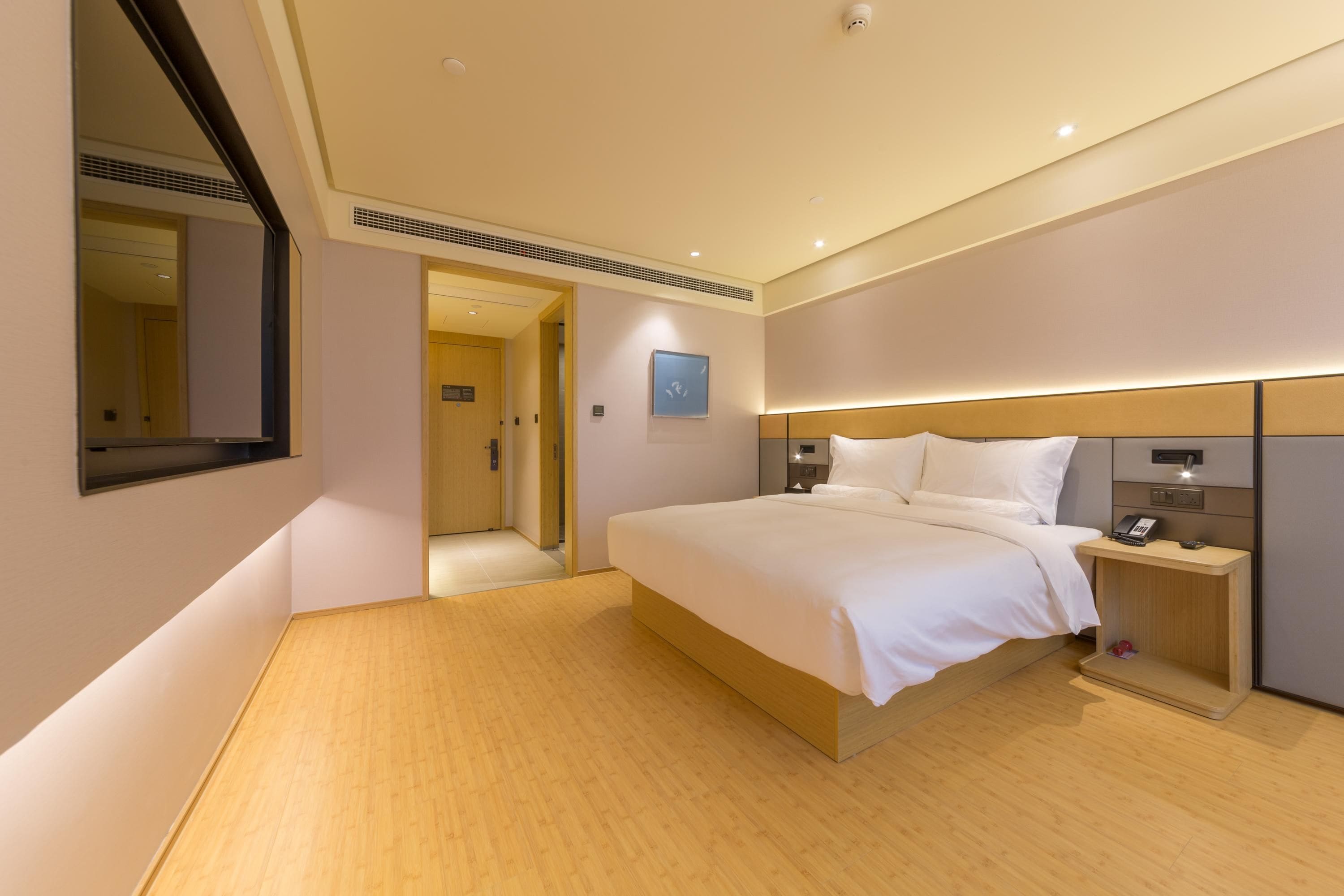 A modern hotel room with a large bed, bedside tables, a mirror, and a door leading to another room.