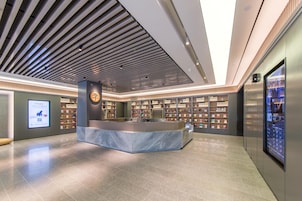 Un vestíbulo moderno con un mostrador de recepción de mármol, estanterías y una pantalla informativa digital.