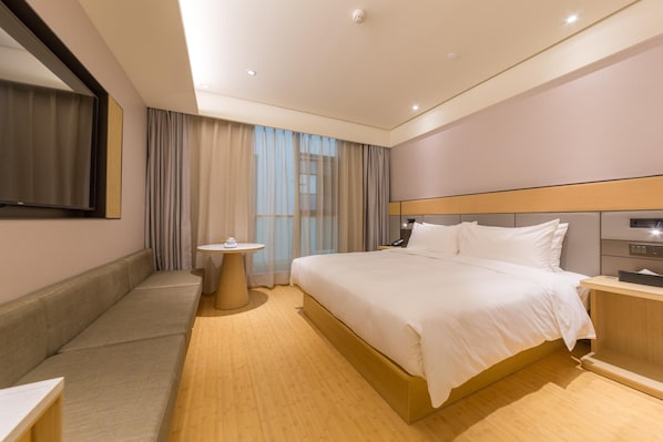 Una habitación de hotel con una cama grande, una mesita de noche, una pequeña mesa redonda, un espejo y una ventana con cortinas.