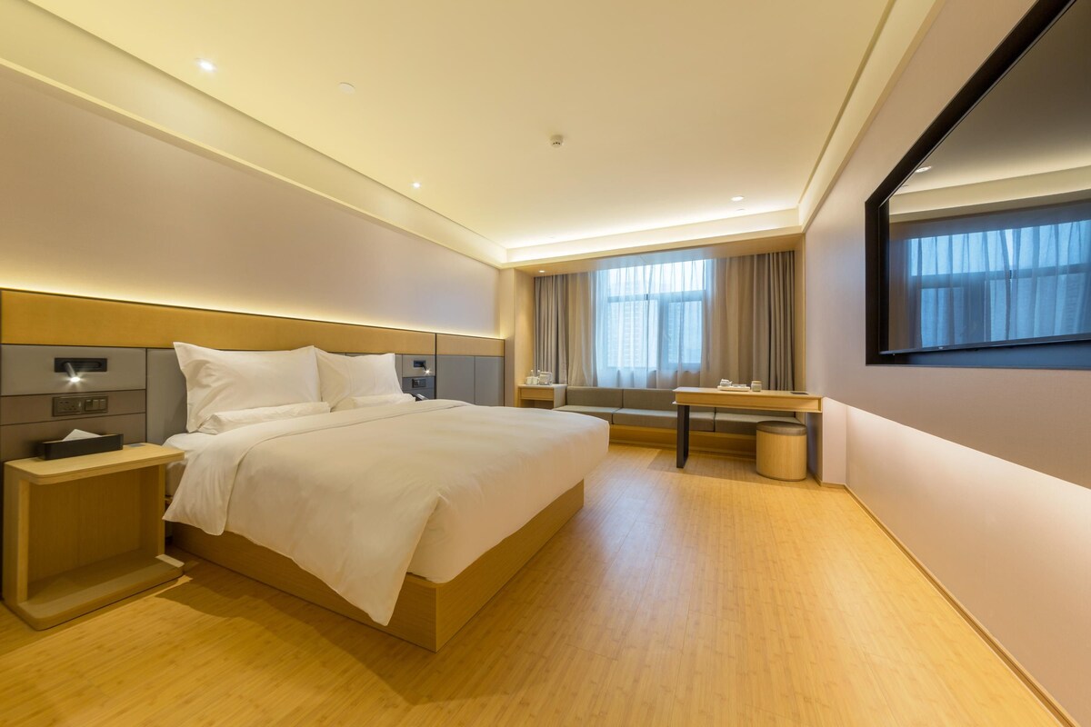 A modern hotel room with a large bed, bedside tables, a desk, and a mirror.