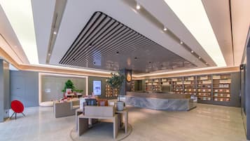 Un moderno vestíbulo de hotel con un mostrador de recepción, zona de estar y una exhibición de libros.