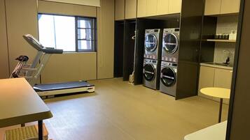 A laundry room with a treadmill, washing machines, and a small sink.