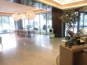 A spacious lobby with a reception desk, a dining area with tables and chairs, large windows, and a potted plant. - Ji Hotel (Wuhan)