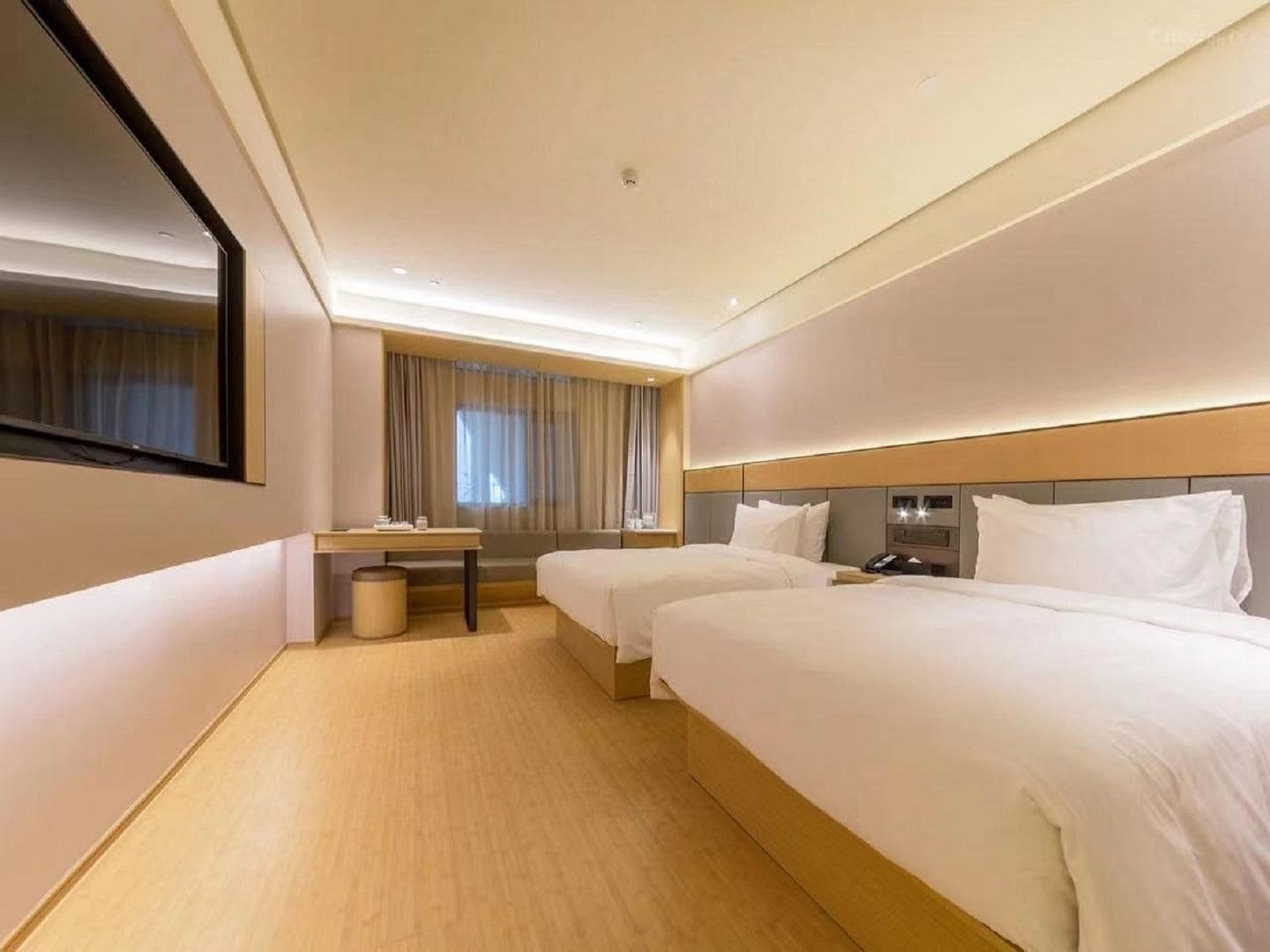 A hotel room with two beds, a desk, a chair, and a large mirror.