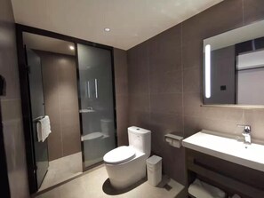 A modern bathroom with a glass shower enclosure, a toilet, a sink, and a mirror. - Hanting Hotel (Beijing)