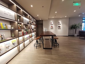 A modern interior with a long wooden table and bar stools, surrounded by bookshelves with various books and decorative items. - Hanting Hotel (Beijing)