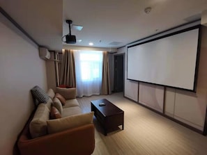 A modern living room with a sofa, a coffee table, a projector screen, and a large window with curtains. - Hanting Hotel (Beijing)