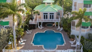 Un resort con piscina rodeada de sillones de descanso, un deck techado y palmeras.