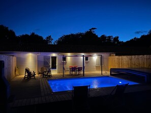 Un patio trasero con piscina, terraza de madera y un área de patio cubierto con mobiliario exterior.
