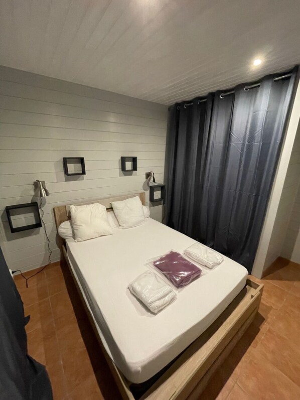Una cama individual con estructura de madera, ropa de cama blanca y una mesita de noche con lámpara.