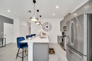 A modern kitchen with a central island, stainless steel appliances, and blue chairs. - Luxe 5BR Townhouse w/ Pool & Mickey-Themed Room (Kissimmee)
