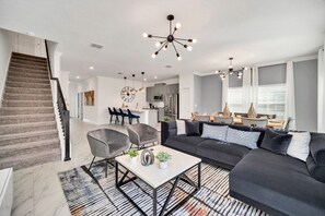 A modern living room with a black sectional sofa, a coffee table, and a staircase leading to another level. - Luxe 5BR Townhouse w/ Pool & Mickey-Themed Room (Kissimmee)