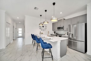 A modern kitchen with a central island, stainless steel appliances, and blue bar stools.