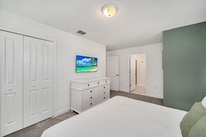 A bedroom with a bed, a dresser, a painting, and a door leading to another room.