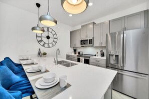 A modern kitchen with a central island, stainless steel appliances, and a clock on the wall. - Luxe 5BR Townhouse w/ Pool & Mickey-Themed Room (Kissimmee)