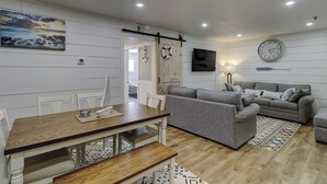 Una sala de estar moderna con un sofá gris, una mesa de comedor de madera y un gran reloj de pared.