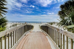 A wooden boardwalk leading to a beach with palm trees on either side.