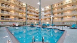 Interior de hotel con piscina, varios balcones y sillones de descanso.