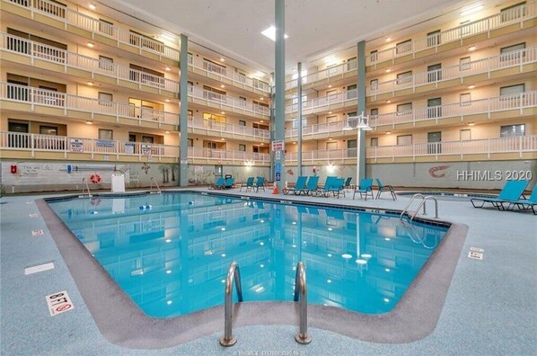 A hotel interior with a swimming pool, multiple balconies, and lounge chairs.